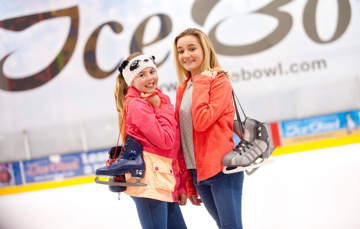 Two Girls with ice skates slung over shoulder at ice rink
