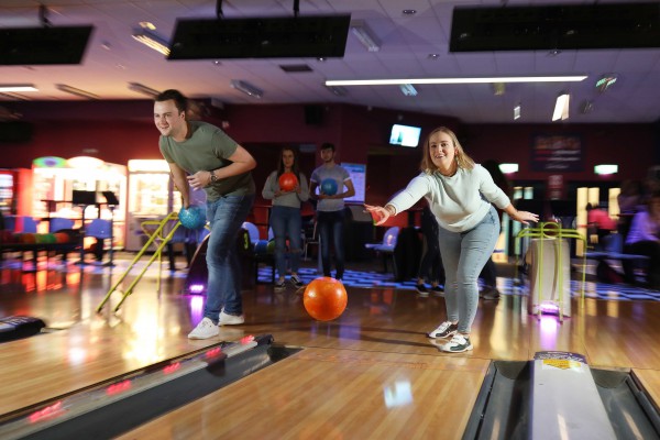 Two people tenpin bowling in dimly lit bowling alley